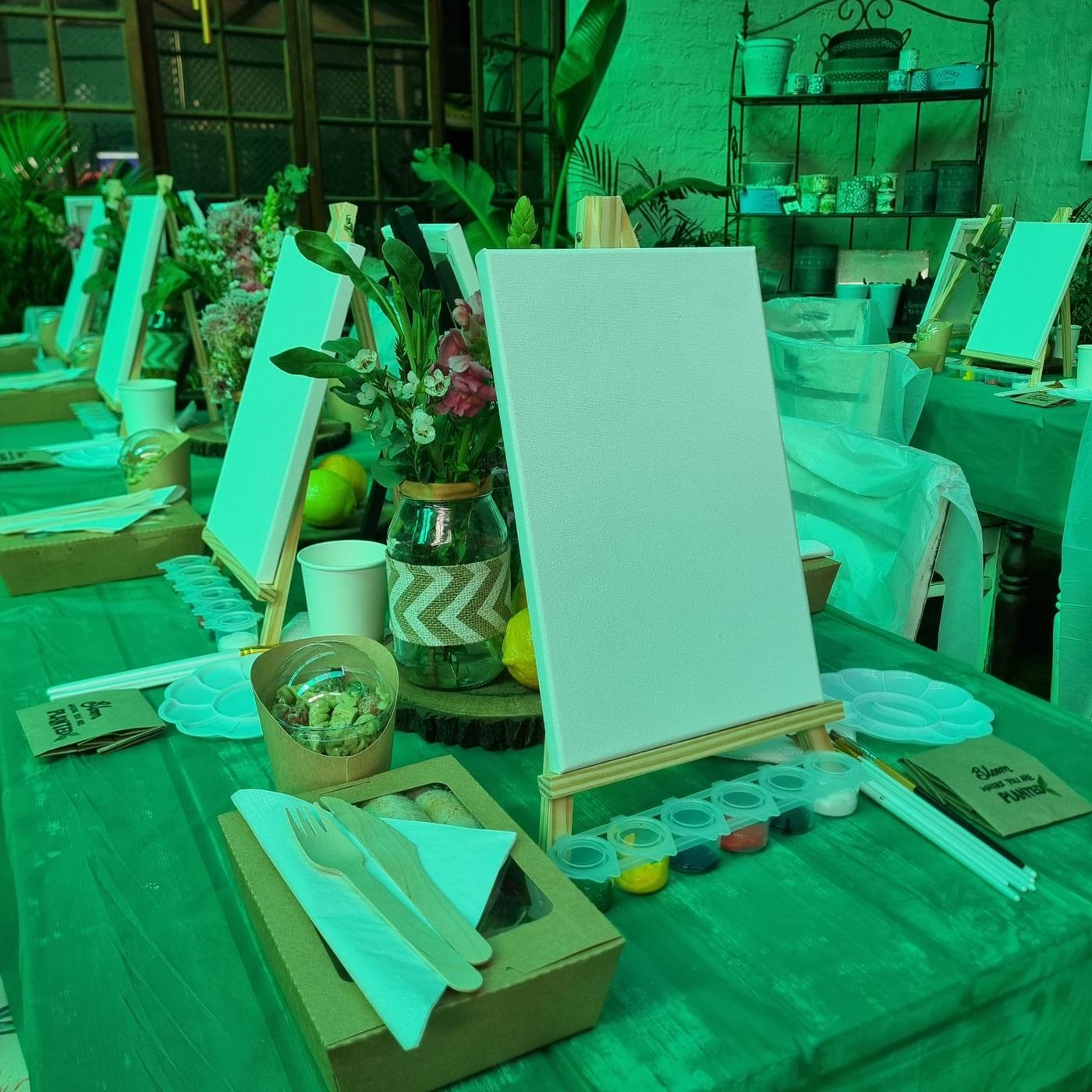 Blank canvases on easels with paint pots, brushes and fresh flowers set out for the Women's Day 2026 Sip & Paint